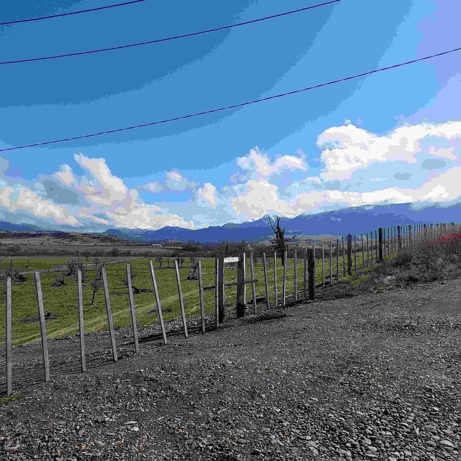 Wooden fence bordering the land parcel, with a gravel road and views of the Patagonian landscape in the background.